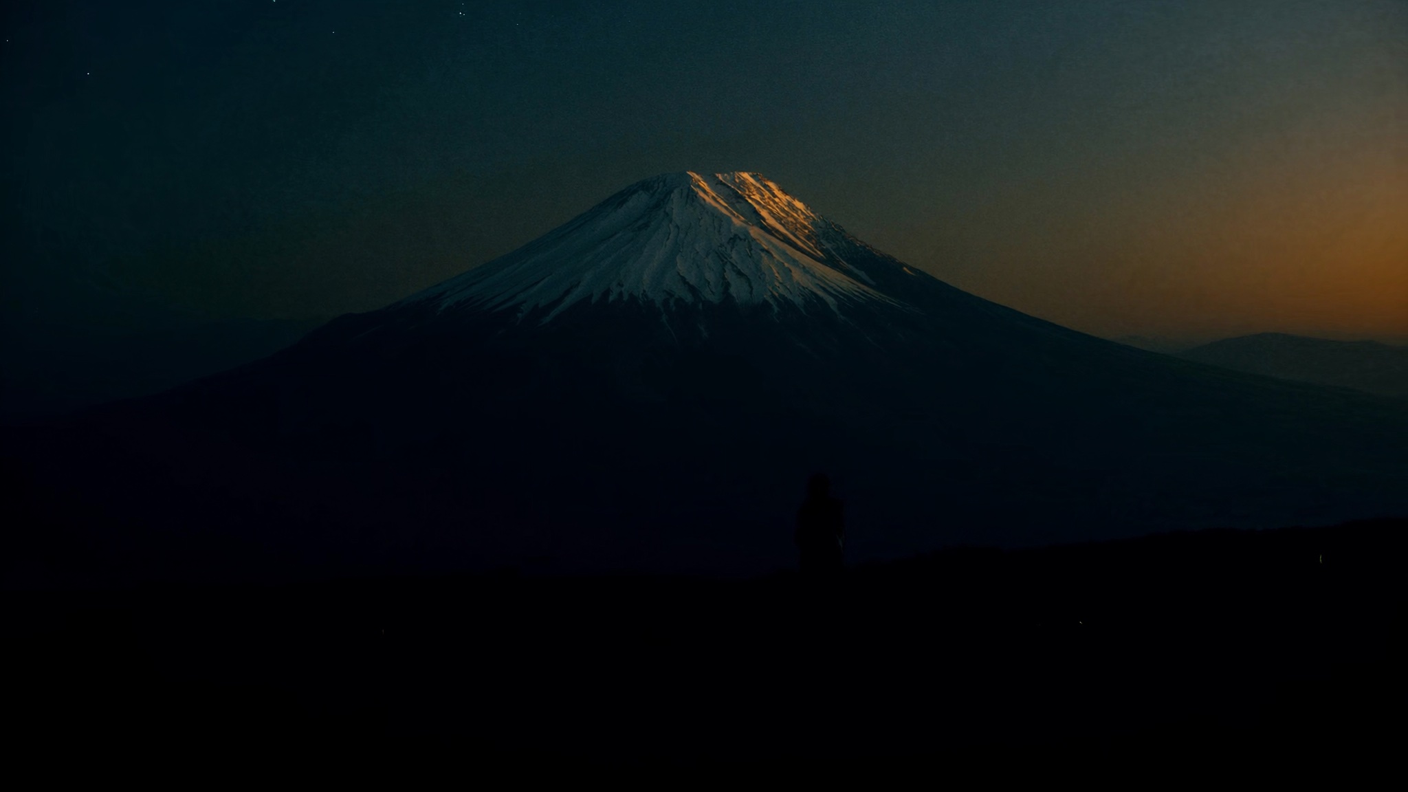 Snow-capped mountain summit catching a warm sunrise glow against a dark dawn sky